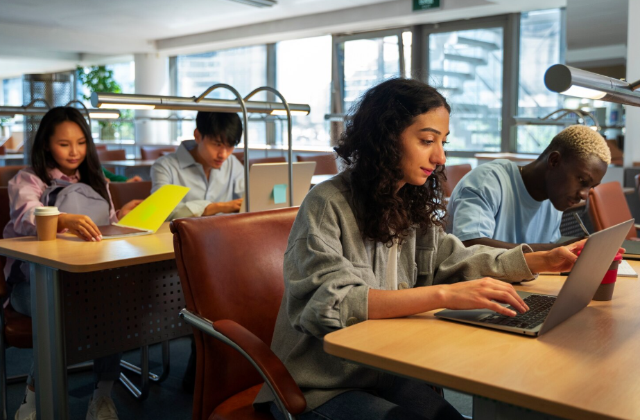 College students studying and working on laptops, balancing academics with work-study responsibilities.