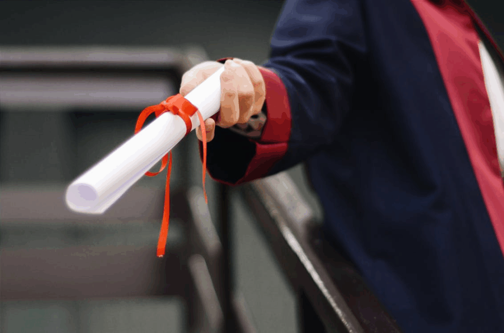 Person in graduation gown holding a rolled certificate with red ribbon