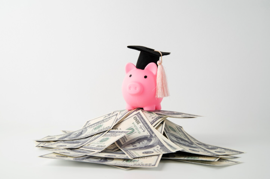 Piggy bank with graduation cap sitting on a pile of dollar bills, symbolizing the hidden costs of education